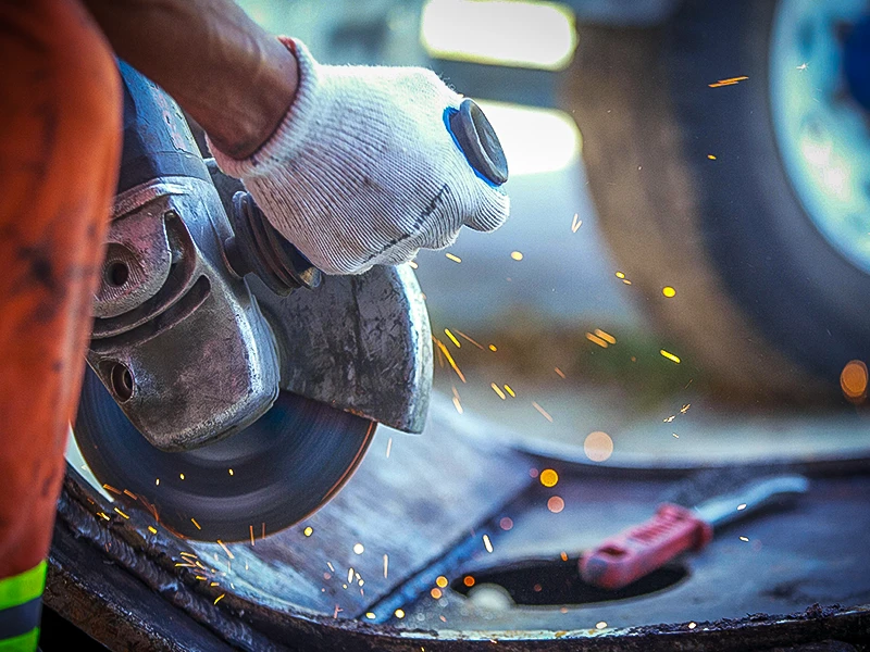 Arbeiter bearbeitet Metall mit einem Winkelschleifer. Werkzeuge gehören im Arbeitsmittelkataster erfasst.