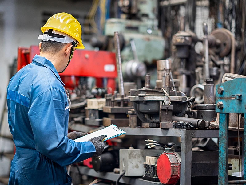 Arbeiter steht mit Clipboard vor einer Maschine. Mit einem digitalen Arbeitsmittelkataster behalten Verantwortliche den Überblick.