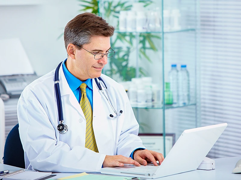 Ein Mann im Arztkittel arbeitet an einem Laptop.