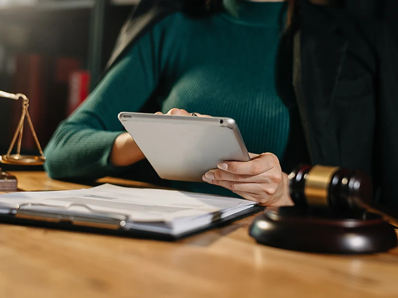 Une femme travaille avec une tablette. À côté d'elle se trouvent un marteau de juriste et une balance. 