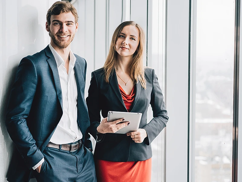 A woman and a man in business attire stand at a pane of glass.