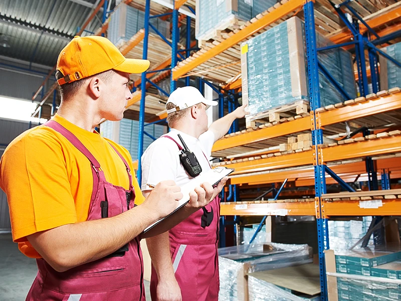 Ein Mann in Arbeitskleidung zeigt seinem Kollegen eine unsicher gelagerte Palette.