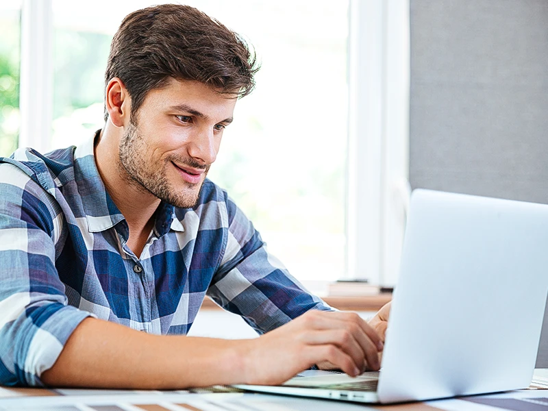 A man in a blue chequered shirt looks at a laptop screen.