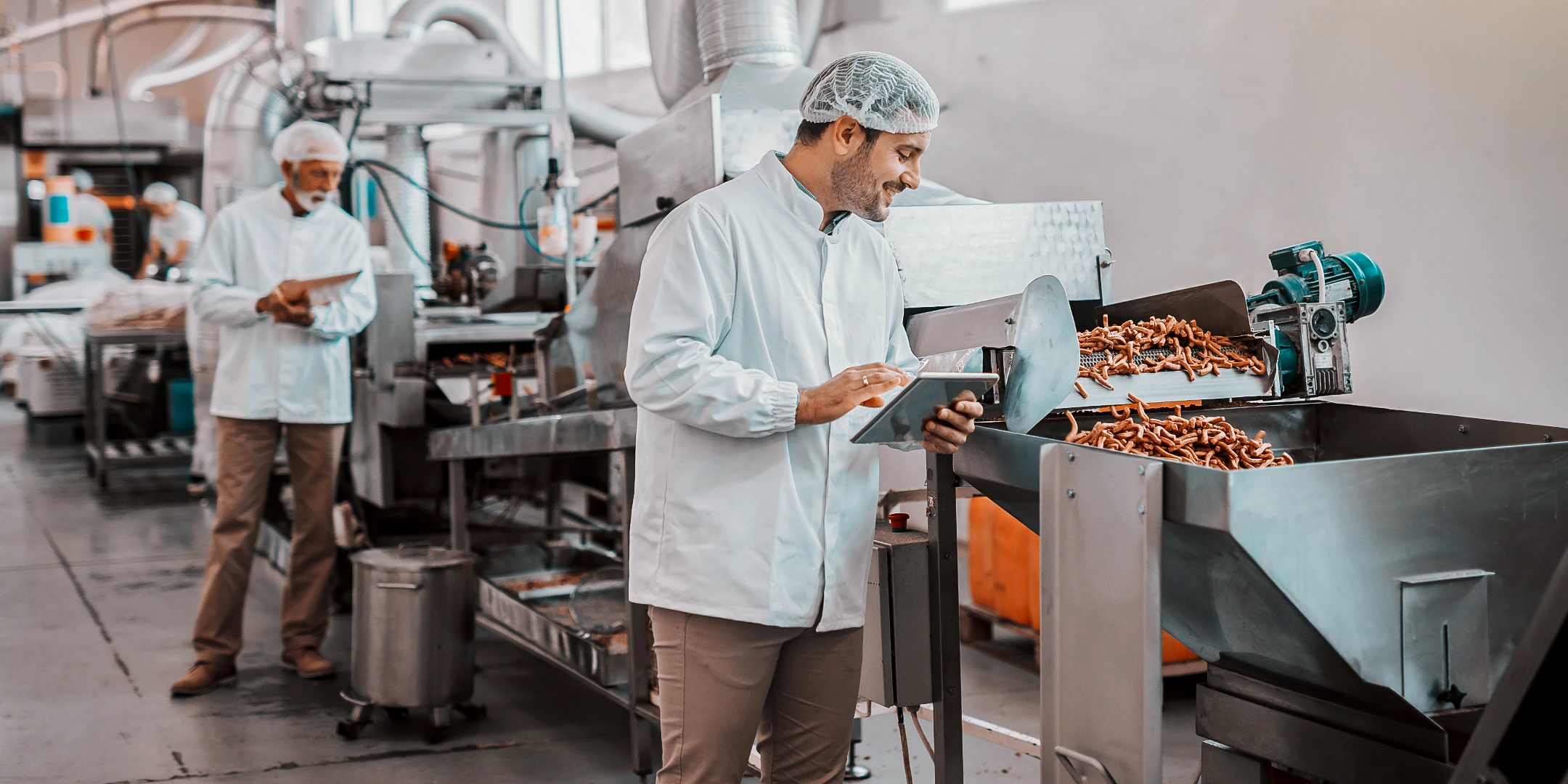 Ein Mann in hygienischer Schutzkleidung bewacht die Produktion von Würstchen