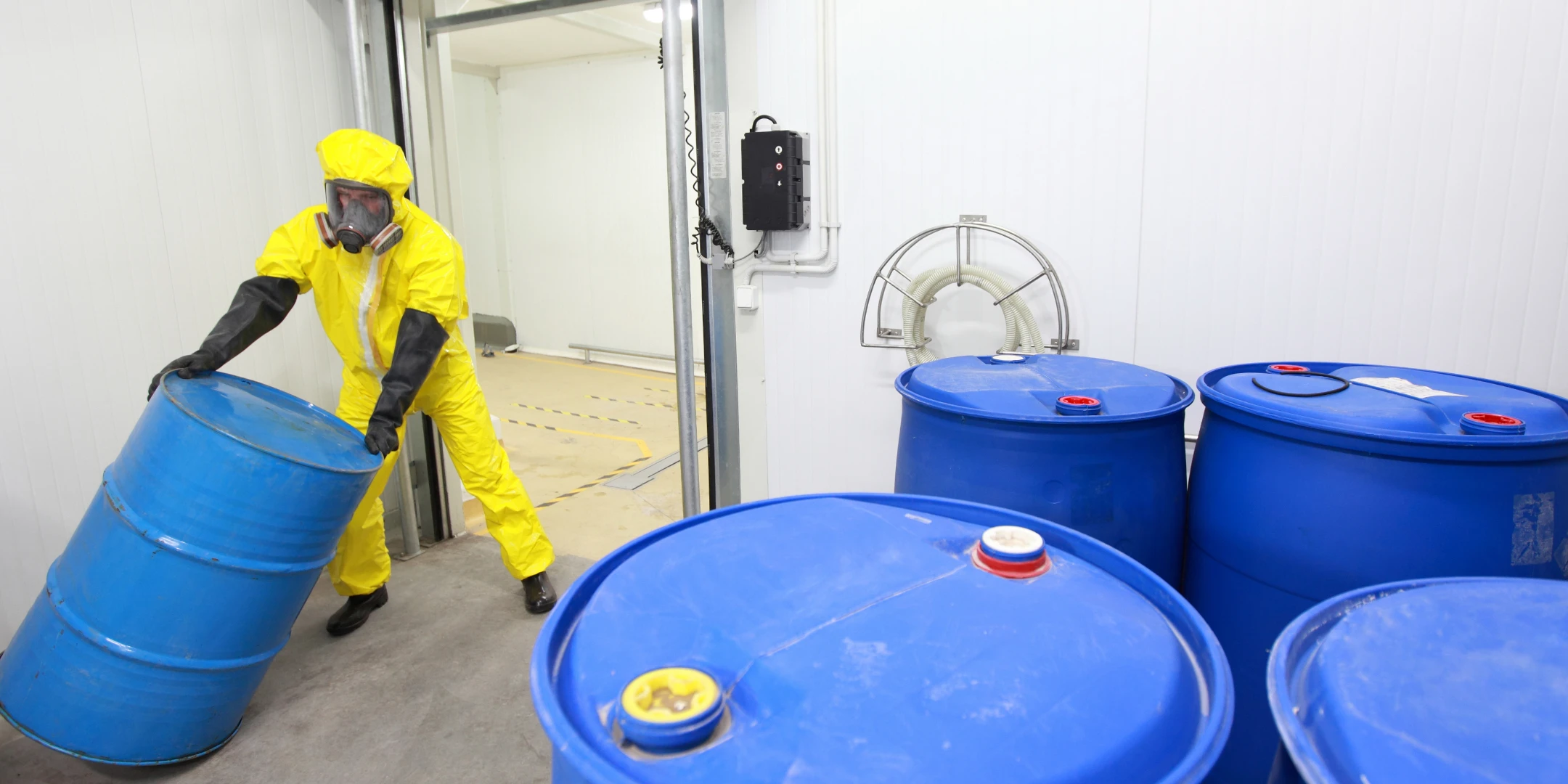 Eine Person in Schutzkleidung bewegt Tonnen mit Gefahrstoffen