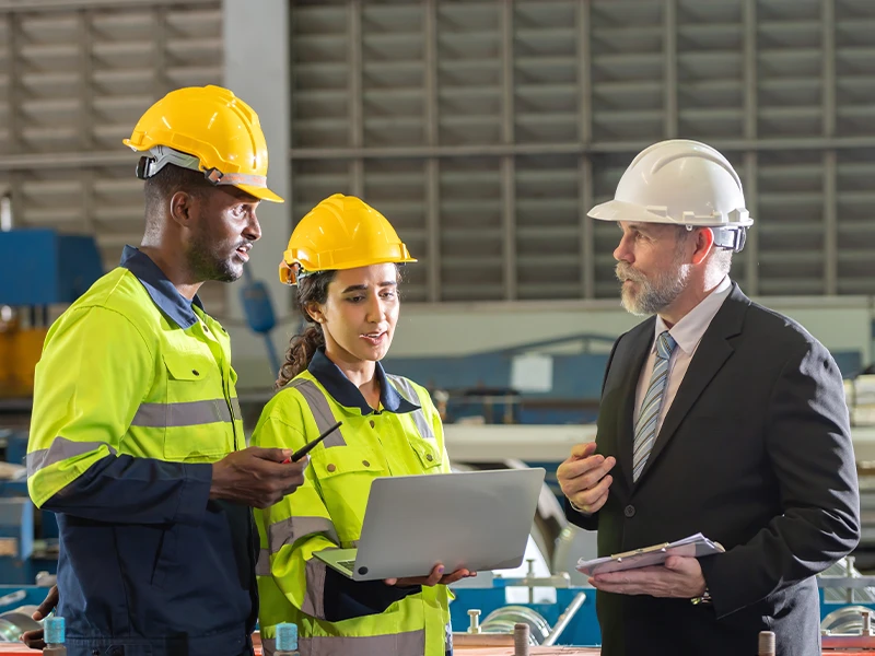 Dwie osoby ubrane w odzież ochronną rozmawiają o czymś z kierownikiem.