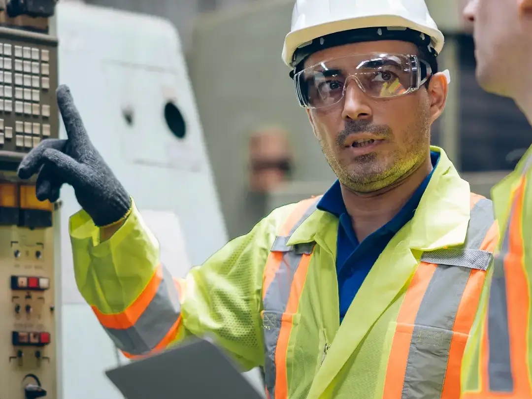 Dwóch mężczyzn stoi przy maszynie z mnóstwem przełączników i przycisków i rozmawia ze sobą.