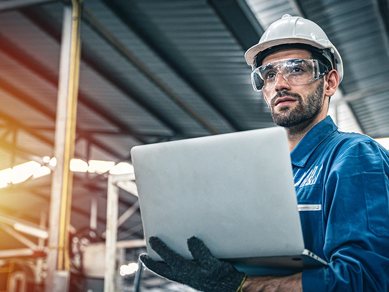 Mann mit Laptop in der Hand und Schutzhelm auf.