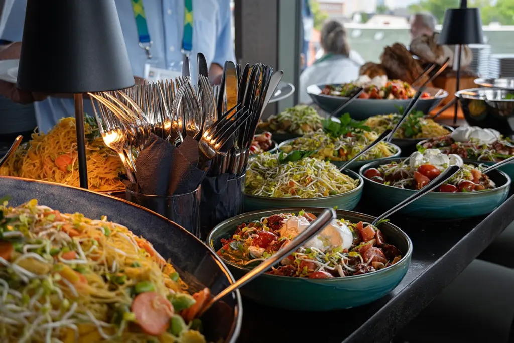 Ein Buffet mit reichem Sortiment bestehend aus Nudeln, verschiedenen Salaten, Brot und dem dazugehörigen Besteck.