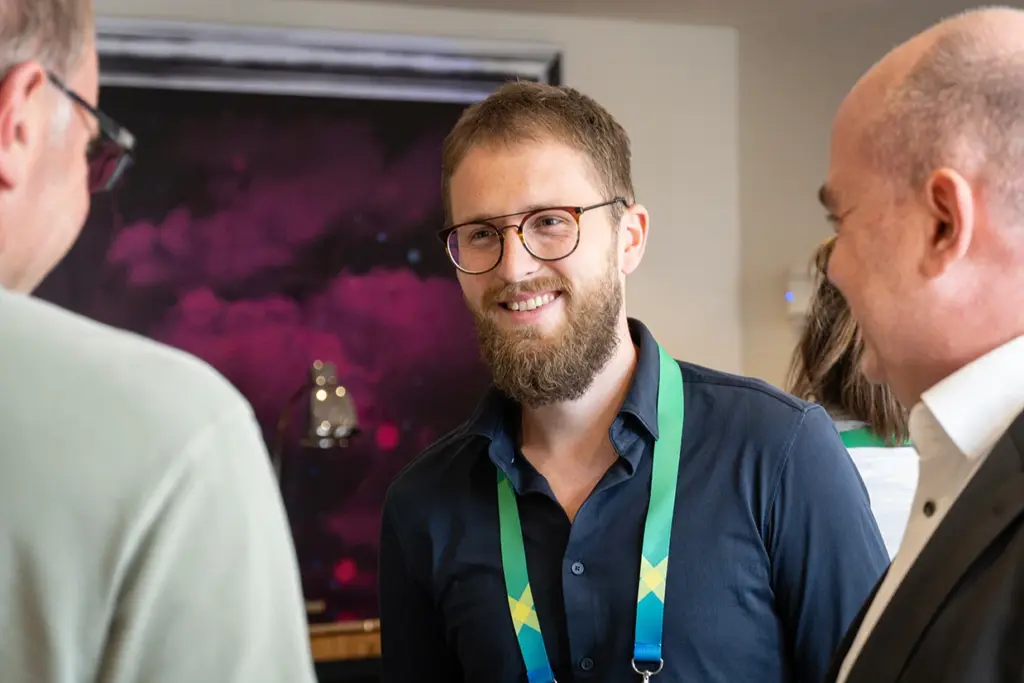 Drei Männer unterhalten sich, mit einem sanften Lächeln, welches eine lockere Atmosphäre impliziert.