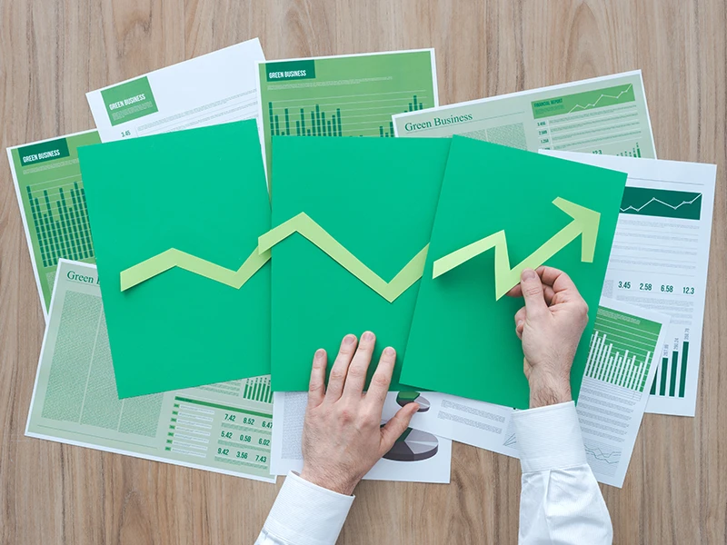 Hände, die grünes Papier in der Hand halten, auf denen Statistiken gezeigt werden.