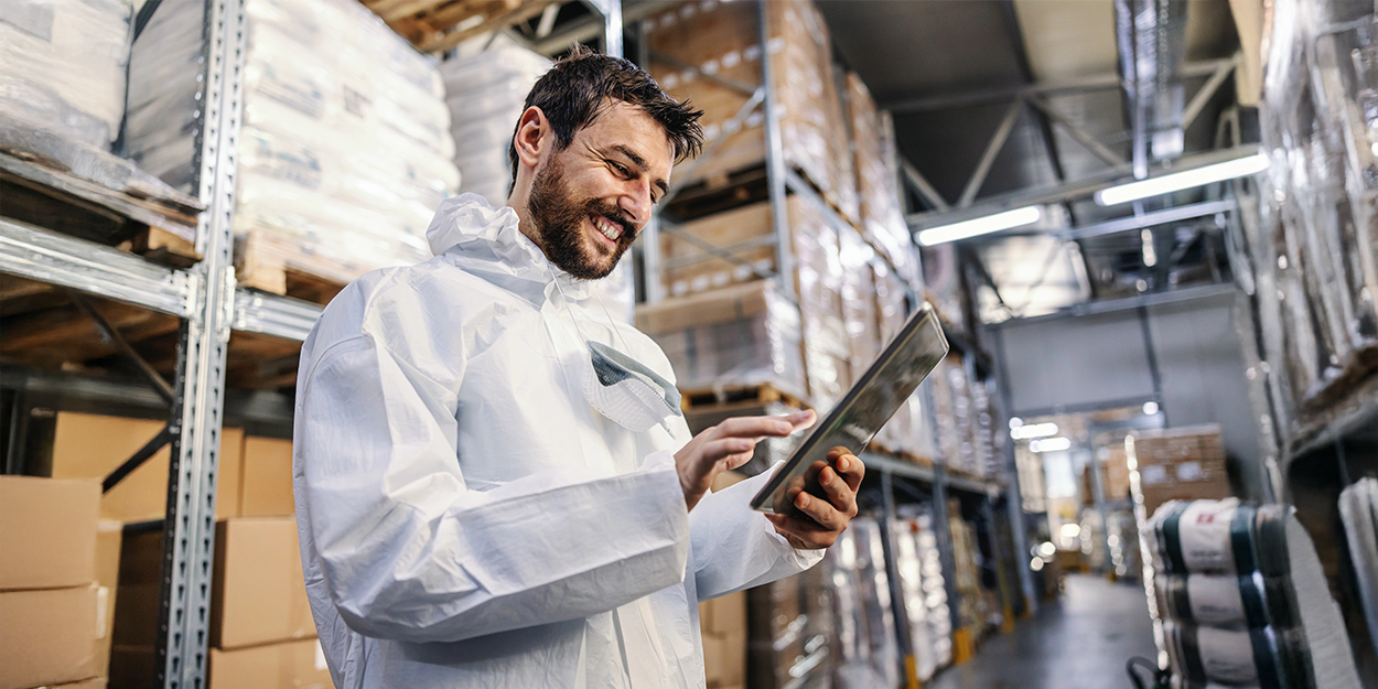 Ein Mann in Schutzausrüstung betätigt in einem Lager ein Tablet