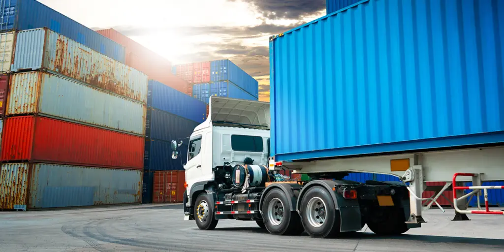 Ein LKW steht auf einem Gelände mit aufeinander gestapelten Containern.