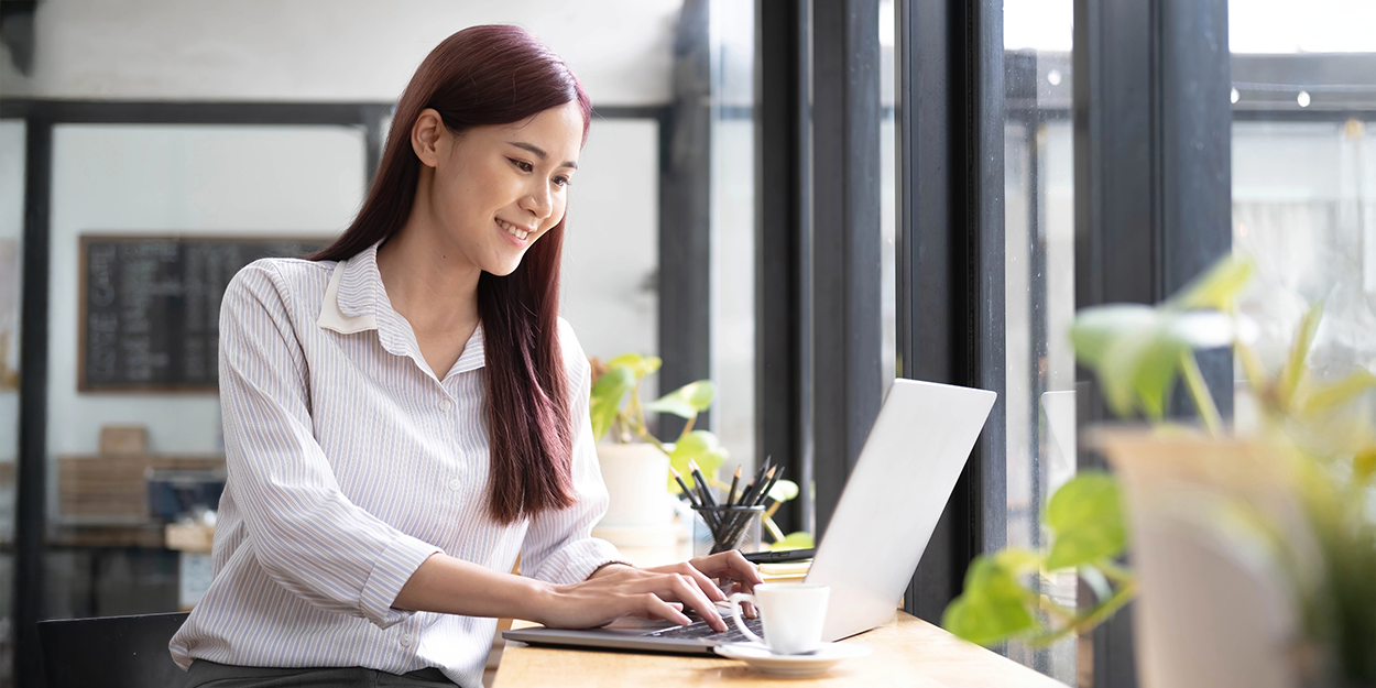 Eine Frau sitzt in einem hellen Büro an ihrem Laptop und trinkt einen Espresso