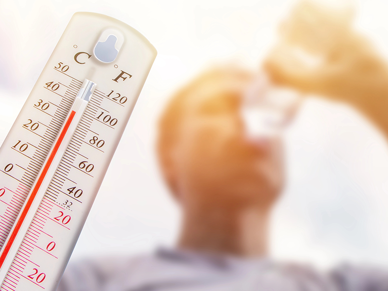 Im Vordergrund ist ein Thermometer, welches 35 Grad anzeigt und im Hintergrund ist ein Mann zu sehen, der Wasser aus einer Flasche trinkt.