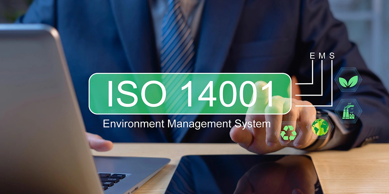 Ein Geschäftsmann arbeitet an einem Laptop und an einem Tablet. Im Vordergrund ist ein grafisches Element, dass ISO 14001 symbolisiert.